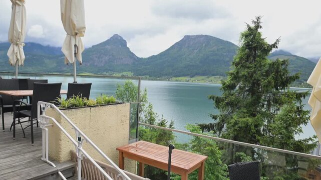 Lakeside restaurant patio overlooking Wolfgangsee with alpine peaks and spring greenery in St. Wolfgang, Austria.