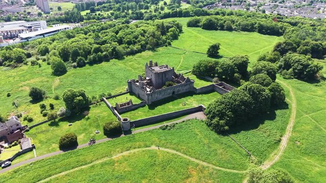 Panoramic wide angle view of old medieval stone castle ruins surrounded by lush green trees and fields in Scotland. Beautiful historic architecture of an ancient fortress on a sunny summer day.