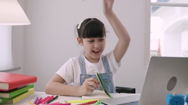 Cute Asian girl student sitting at desk using a laptop computer for studying online learning via video calling with remote teacher in a home school. Homeschooling education and new normal concept. 