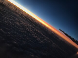 Obraz premium Sunset above the clouds view from airplane window A breathtaking view of a vibrant golden sunset above a thick layer of clouds, taken from a commercial airplane window with a wing