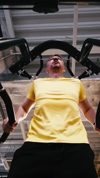 Man Performs Assisted Dips On Parallel Bars In The Gym With Legs Supported, Viewed From Below, Vertical Video