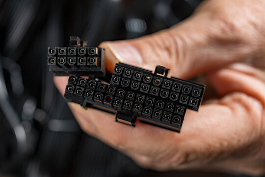 Computer power supply connectors in hand, Closeup of a hand holding black ATX 24 pin and CPU power connectors for a PC hardware assembly