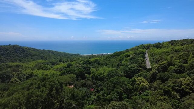Aerial drone shot moving out from the lush vegetation of the Pacoche Marine Coastal Wildlife Refuge, revealing the scenic Spondylus highway road and the vibrant blue Pacific Ocean on the horizon. Capt