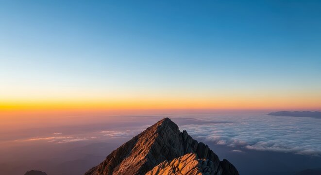 A breathtaking view from a jagged rocky summit peak high above the clouds under a clear blue sky at dawn, environment, wilderness, scenic