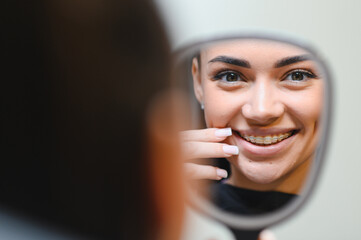 Young woman smiling with braces in mirror reflection