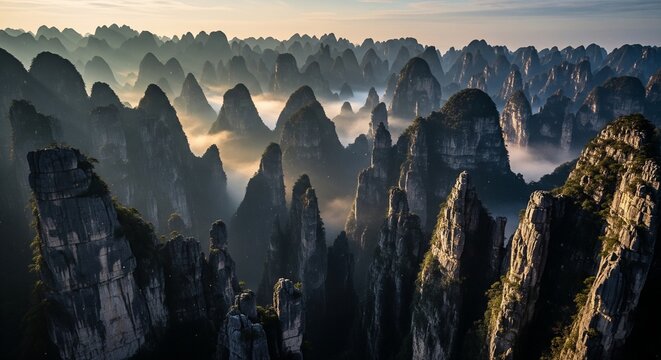 Spectacular view from above of endless mountain peaks surrounded by white fog at sunrise. Early morning sunlight hits the side of the rocky hills, showing texture and deep valleys
