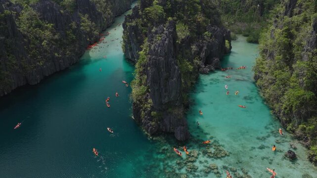 Aerial view of Big Lagoon with tourists in kayaks navigating turquoise waters between towering limestone cliffs and lush greenery in El Nido, Mimaropa, Philippines.