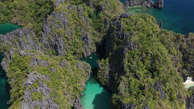 Aerial view of Big Lagoon limestone cliffs and turquoise waters with small kayaks navigating the narrow entrance in El Nido, Mimaropa, Philippines.