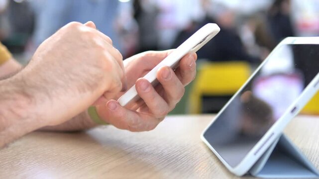 Hand taps smartphone. Tablet rests nearby. Focus on digital interaction. Casual setting, relaxed posture. Ideal for tech, communication, or business themes