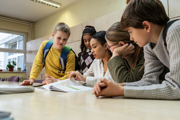 A small group of students is in their elementary classroom while a mixed-race teacher guides them...