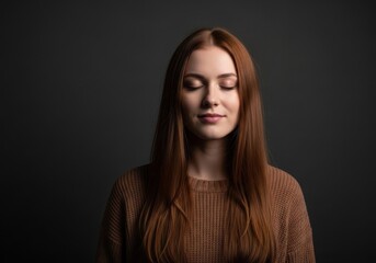 Naklejka premium Portrait of a serene young woman with long red hair and closed eyes, wearing a brown knitted sweater, meditating or relaxing against a dark background