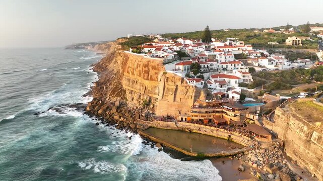Aerial view of Azenhas do Mar village with white houses perched on a steep cliff overlooking the Atlantic Ocean and a natural pool in Colares, Lisbon, Portugal.