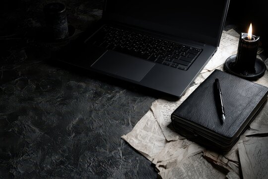 A dark and moody scene with a laptop, a lit candle, and an open journal with a pen on aged paper.