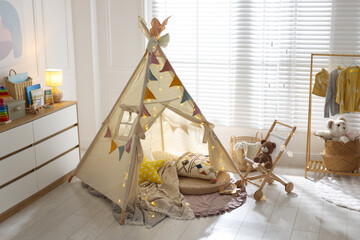 Cute wigwam with fairy lights and toys in stylish child's room © New Africa