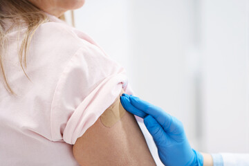 Fototapeta premium Doctor in medical gloves applying adhesive bandage onto patient's arm after vaccination in hospital, closeup