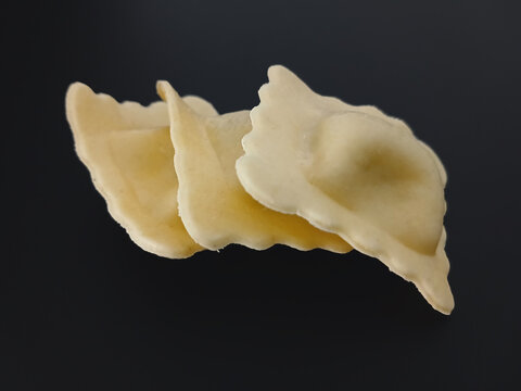 Three ravioli isolated on a black background. Close-up of raw, square, filled fresh pasta. Healthy eating.
