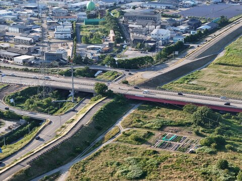Aerial view of urban landscape with busy highway and bridge. Green fields border roads and residential zones. Vehicles move steadily under modern infrastructure