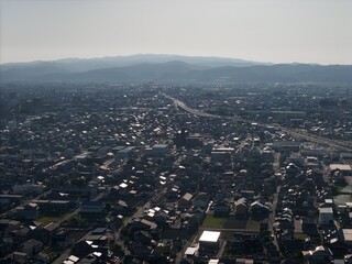 Fototapeta premium Aerial view captures sprawling urban landscape under soft haze. Distant hills frame the city's quiet expanse, serene and calm. Buildings cluster in orderly rows, streets fade into subtle blur
