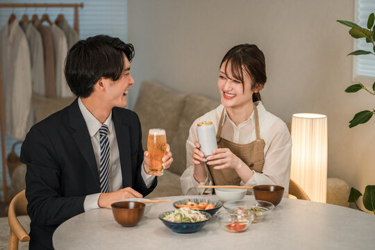 A young Asian couple (beer, canned beer) eating and drinking at their dining table in their home.