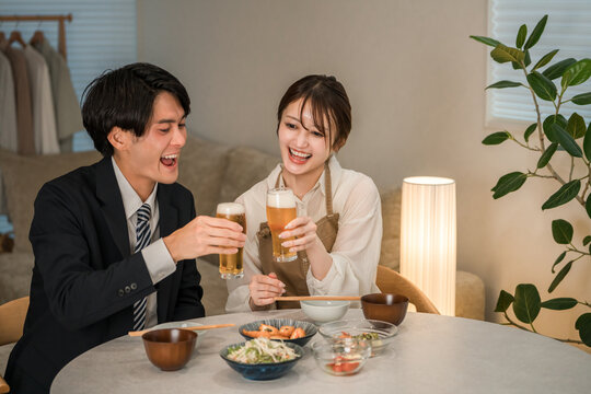 A young Asian couple enjoying a meal and drinks at their dining table in their home.