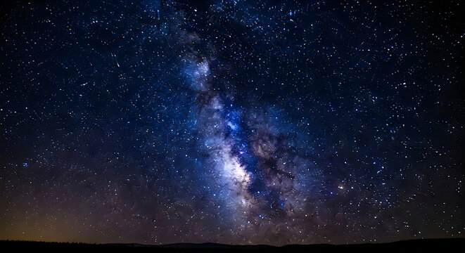 Bright milky way galaxy shining with countless shimmering stars in the deep dark blue night sky above the quiet horizon