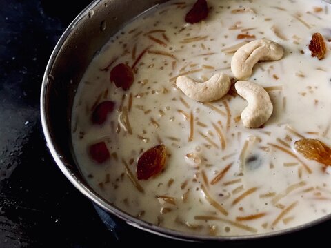 Vermicelli pudding or khir or semiya payasam topped with dried grapes and nuts, served chill in a bowl with black textured background, Traditional Arabic Indian festive dessert.