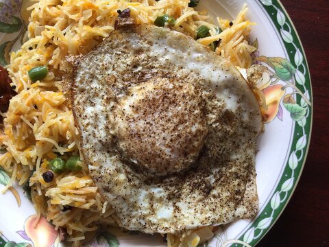 Vermicelli semiya cooked with vegetables and fried egg sunny side up on a plate. Indian breakfast food texture, close up.