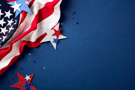 American flag draped on the left and patriotic red, white, and blue glitter stars. Navy blue textured background with copy space for 4th of July or Memorial Day.