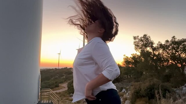 Carefree woman flipping her hair at sunset wind farm