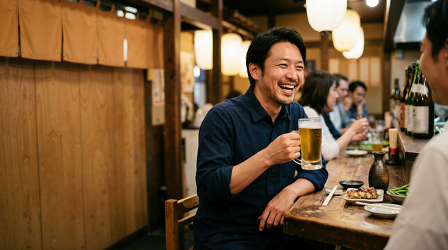 Laughing Japanese man drinking beer at an izakaya counter. Happy male enjoying drinks and yakitori with friends in a traditional pub