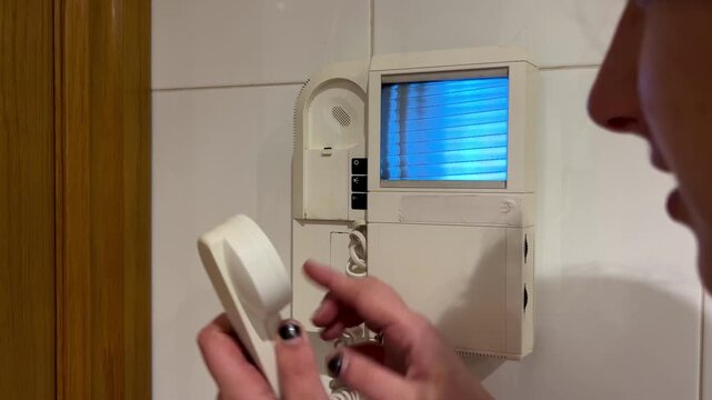 Woman answering an old video intercom call and opening the building front door