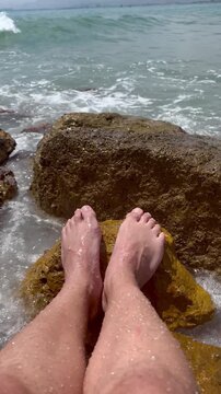 Point of view of male feet on a rock with waves splashing