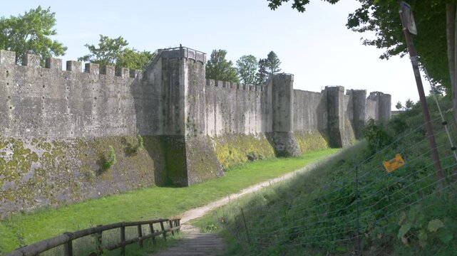 Ancient stone fortress wall with defensive towers and a grassy moat on a bright sunny day.