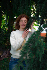 Naklejka premium Thoughtful woman gently touching green leaves in a lush natural setting. Concept of mindfulness, wellbeing, harmony with nature, self-discovery and peaceful outdoor living.