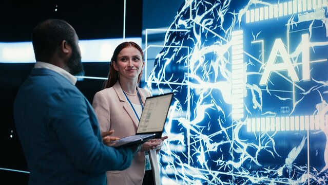 Team of engineers monitors progress of artificial intelligence neural network evolution using laptop, Teamworking colleagues observing rapid development of AI machine learning tech, camera B.