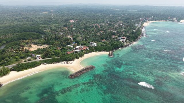 Aerial view of the tropical coastline with sandy beaches, turquoise water, and a stone breakwater, Peraliya, Southern Province, Sri Lanka.