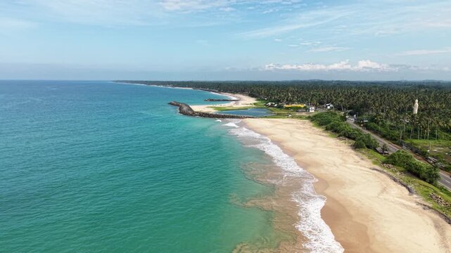 Aerial view of the sandy coastline with the Tsunami Memorial Buddha Statue and a stone breakwater in Peraliya, Southern Province, Sri Lanka.