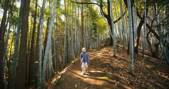 Happy child walking down dirt path surrounded by bamboo thicket - steady cam backwards
