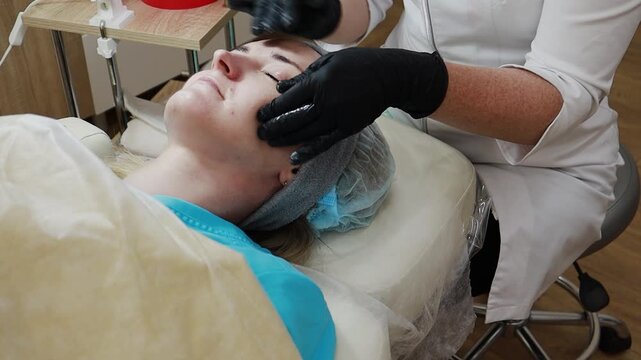 A female doctor, a professional cosmetologist, prepares a patient's face for a procedure