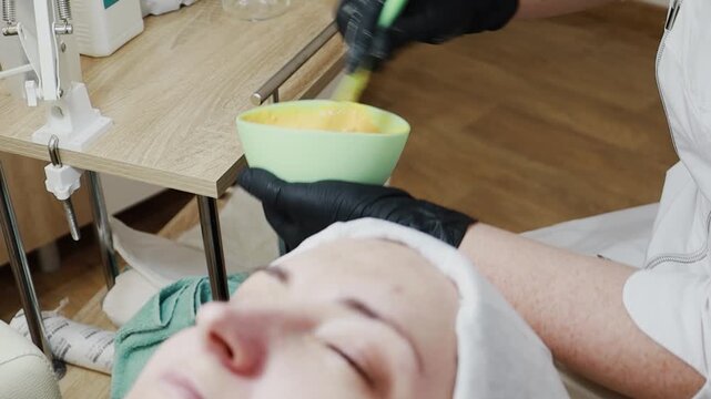 A female doctor, a professional cosmetologist, mixes a mask for application to a patient's face