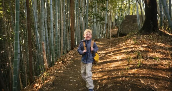 Joyful child with backpack walking on path through bamboo grove in Japan - steady cam shot