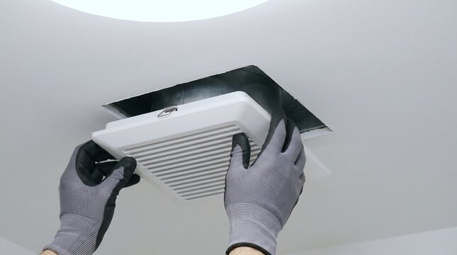 Technician hands installing white bathroom exhaust fan cover in ceiling close up