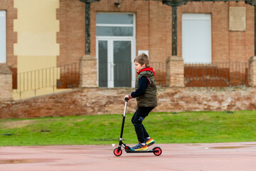 Child uses scooter in playground near brick building on a cloudy day © Luis