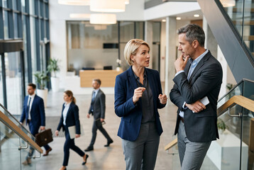 Fototapeta premium Corporate colleagues talking while standing on staircase in modern office lobby