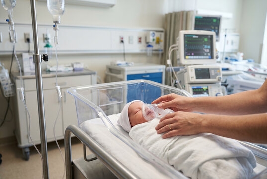 Medical nurse caring for newborn baby in hospital maternity ward bassinet