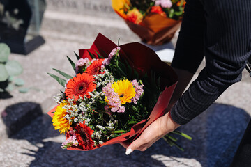 Obraz premium Woman placing flower bouquet on grave. Cemetery memorial visit. Remembrance and mourning tradition. Colorful flowers during commemoration ceremony closeup.