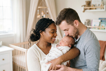 Fototapeta premium Diverse young parents lovingly holding their newborn baby in a bright clean home nursery