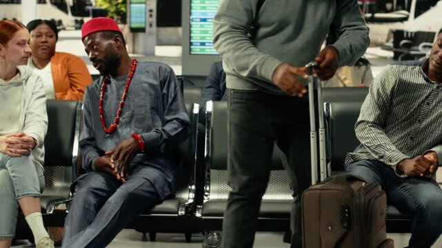 Diverse men travelers in modern station hall waiting for interstate departures. Group of passengers carrying baggage and carry-on bags review route schedule and timetable, long-haul travel.