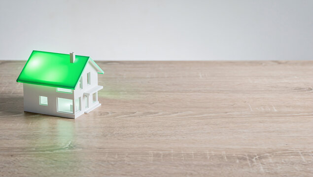 Small white architectural model of house with glowing green roof on wooden table over plain background