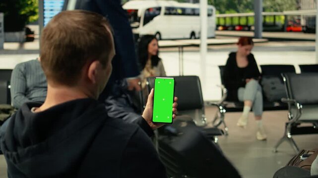 Vertical chroma key on smartphone in modern bus station with seated passengers waiting for daily commute. Diverse people on the move creates realistic public transportation activity.